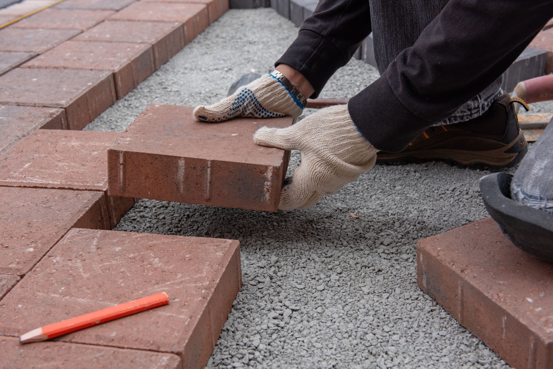Installing paver bricks for patio in backyard. A workman's gloved hands use a hammer to place stone pavers.